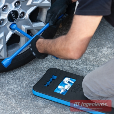 Mecánico aflojando tornillos con llave en cruz sobre alfombra de rodillas profesional