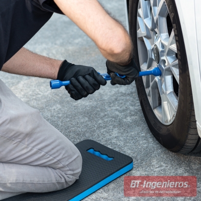 Persona usando alfombra de rodillas para taller mientras afloja tornillos de rueda