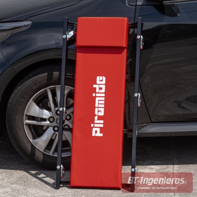 Camilla de taller Piramide plegada verticalmente junto a un coche.