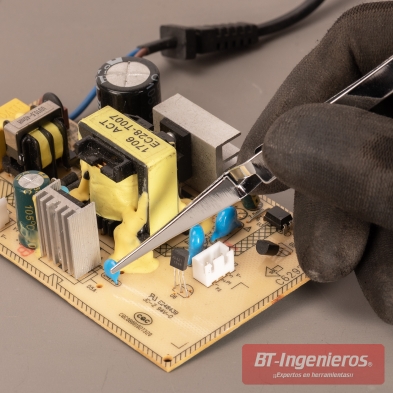 Pinza de precisión manipulando un componente en una placa electrónica, sujetada con guante de trabajo