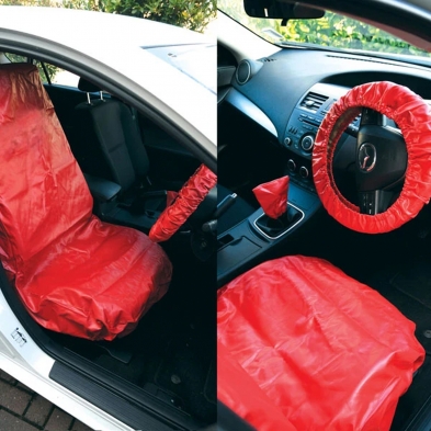 Fundas protectoras rojas colocadas sobre asiento, volante y palanca de cambios en el interior de un coche