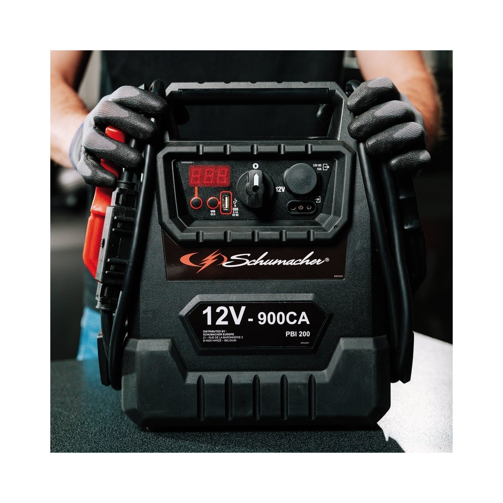 Booster Schumacher 12V 900CA en uso, con empuñadura ergonómica y cables de arranque profesionales.